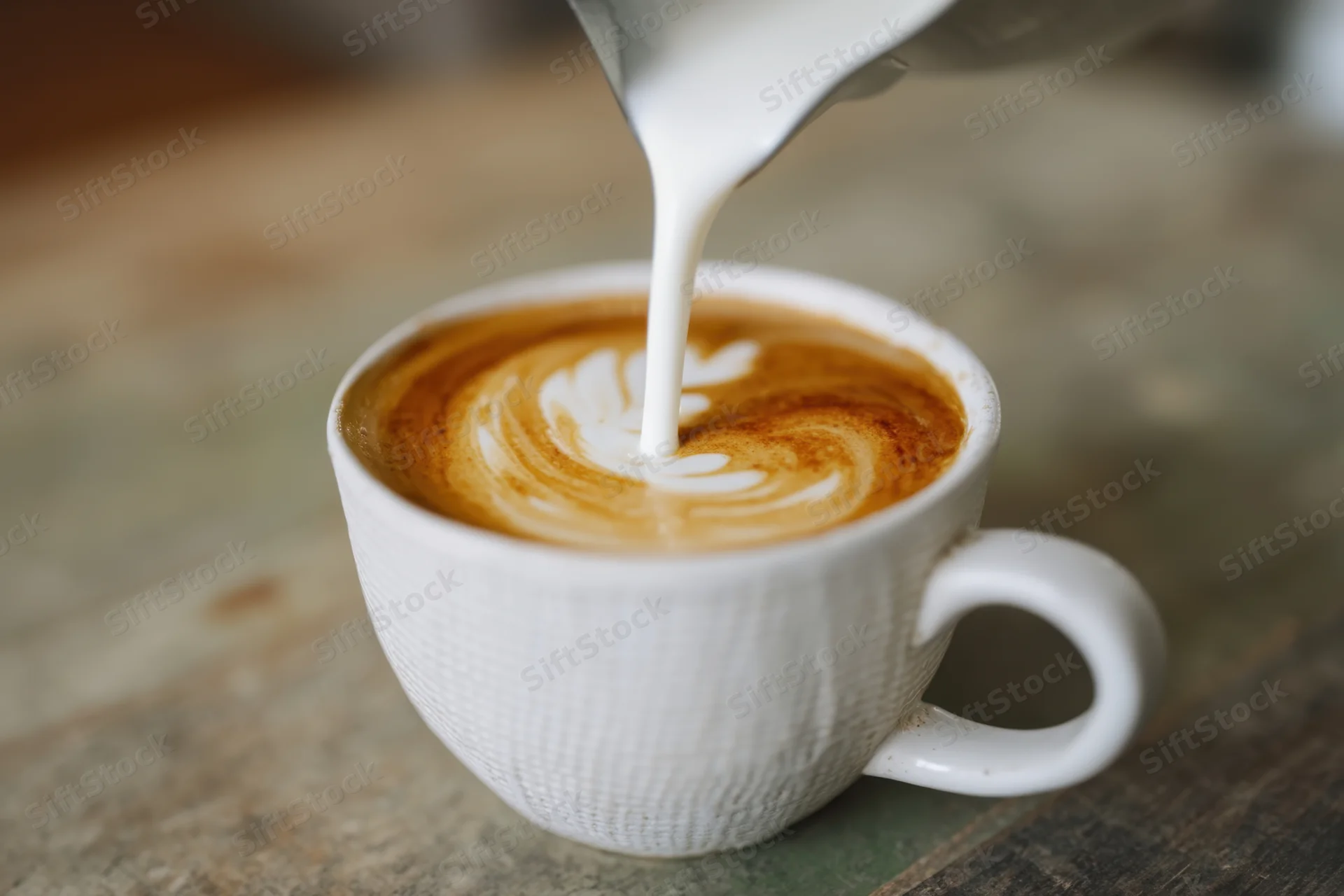 Milk being poured into a latte to create latte art in a white ceramic cup on a wooden table