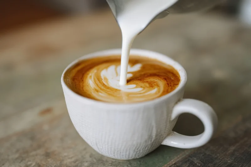 Milk being poured into a latte to create latte art in a white ceramic cup on a wooden table