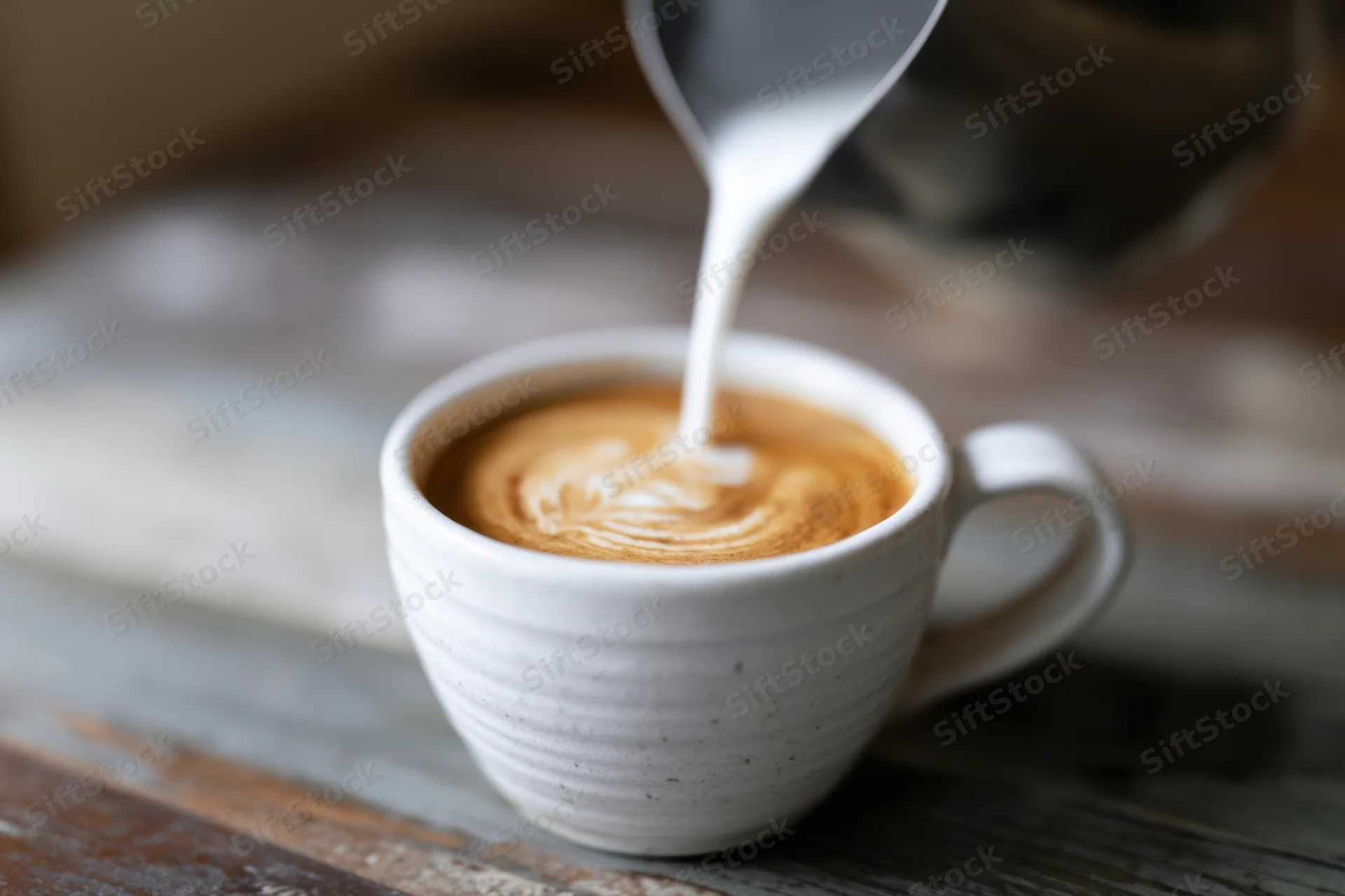 Milk being poured into a latte to create latte art in a ceramic cup on a wooden table