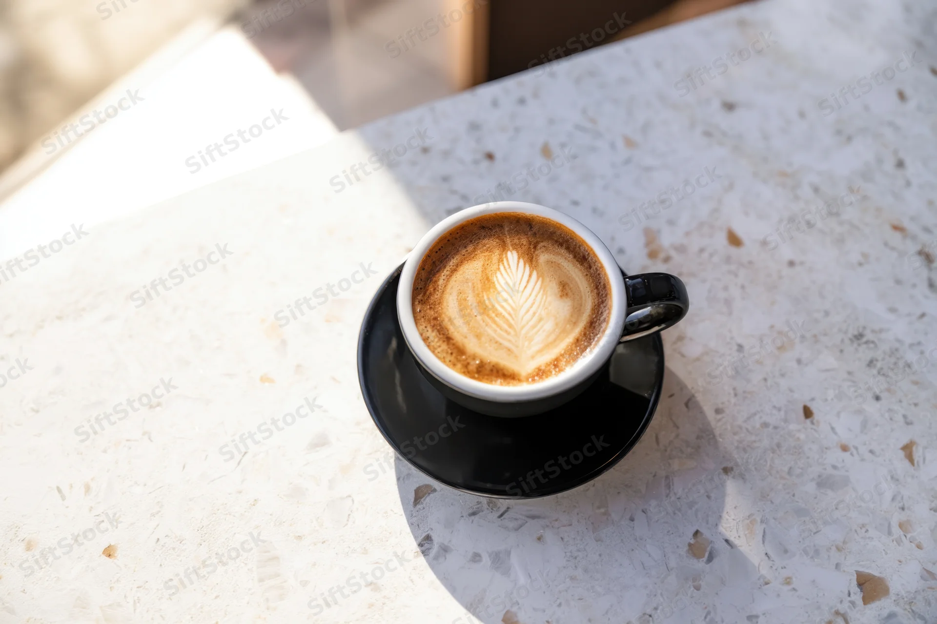 Freshly poured latte with leaf-shaped foam art on a marble tabletop outdoors in sunlight