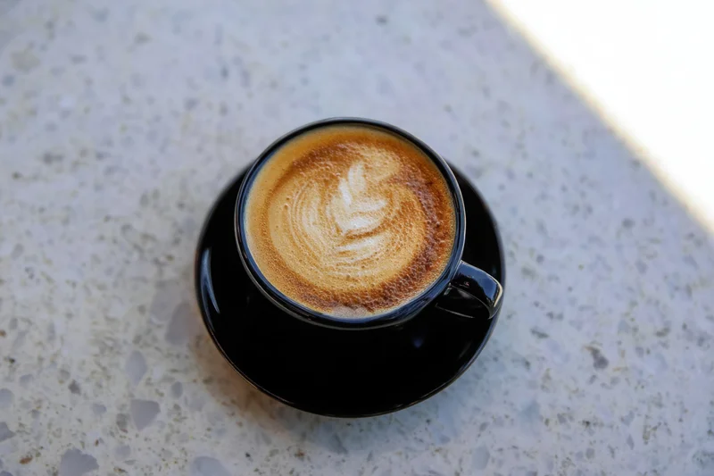 Freshly poured latte with heart-shaped foam art in a black cup on a terrazzo tabletop