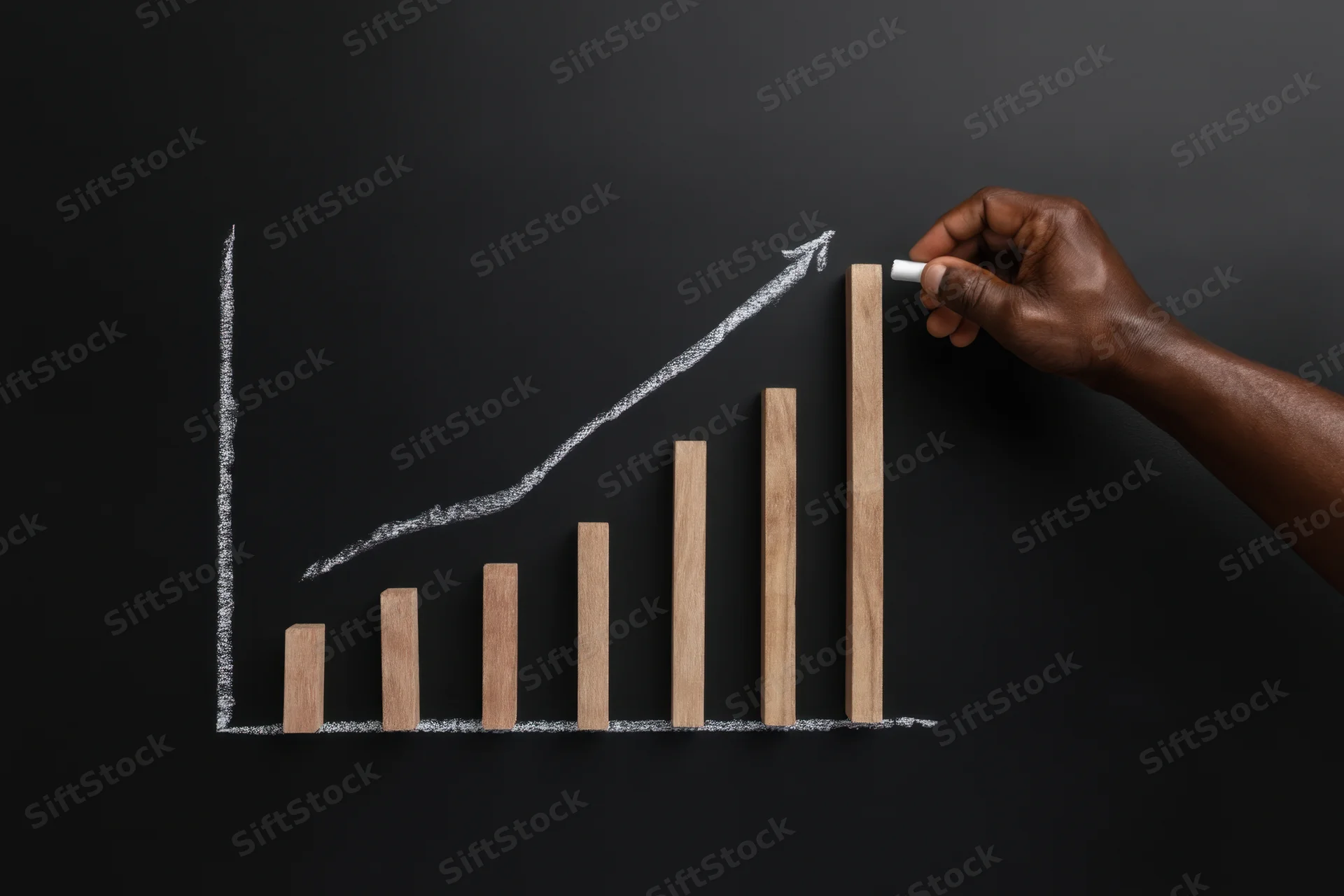 Hand drawing upward growth chart with chalk on blackboard using wooden bars as data points