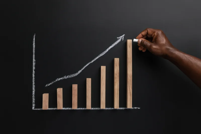 Hand drawing upward growth chart with chalk on blackboard using wooden bars as data points