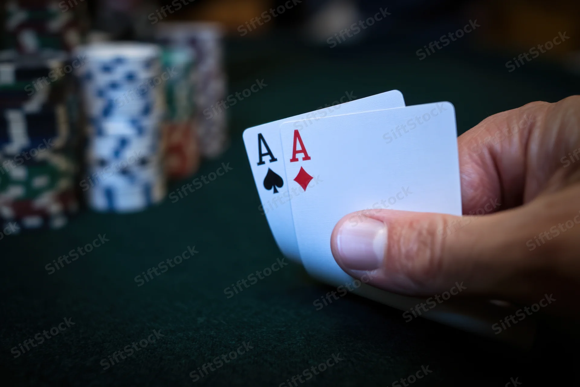 Hand holding two aces over green felt poker table with stacks of casino chips in background