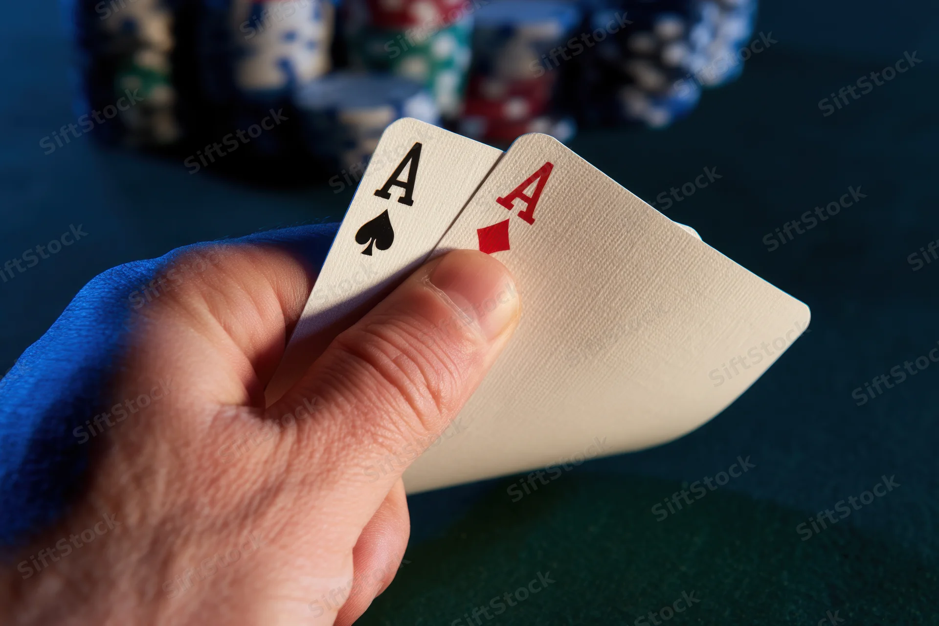 Hand holding two aces, spade and diamond, over green felt table with poker chips in background
