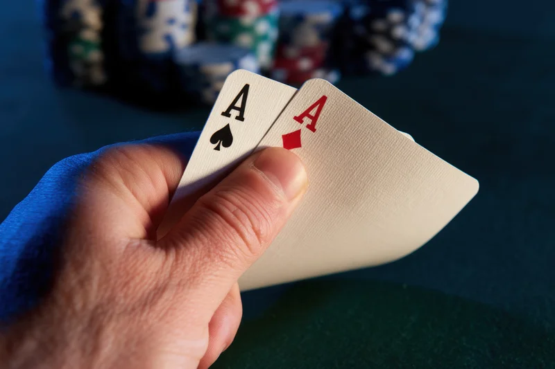 Hand holding two aces, spade and diamond, over green felt table with poker chips in background