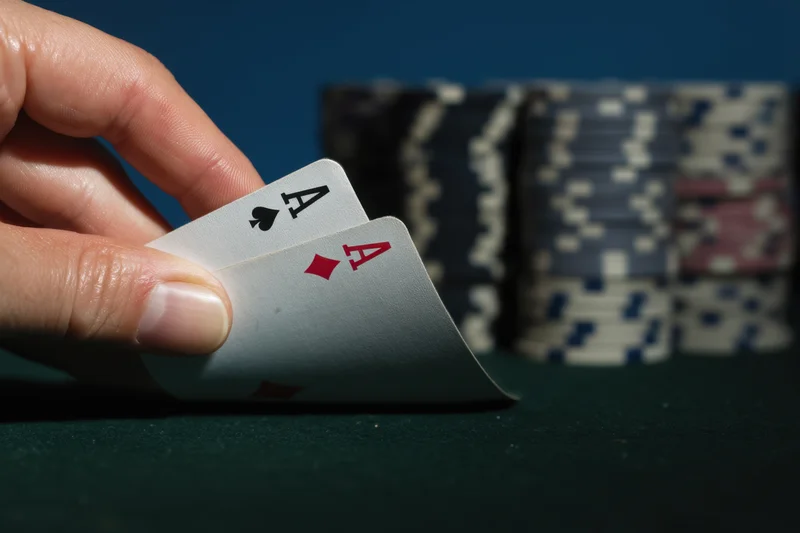 Hand holding two aces on a green felt poker table with stacks of chips in the background
