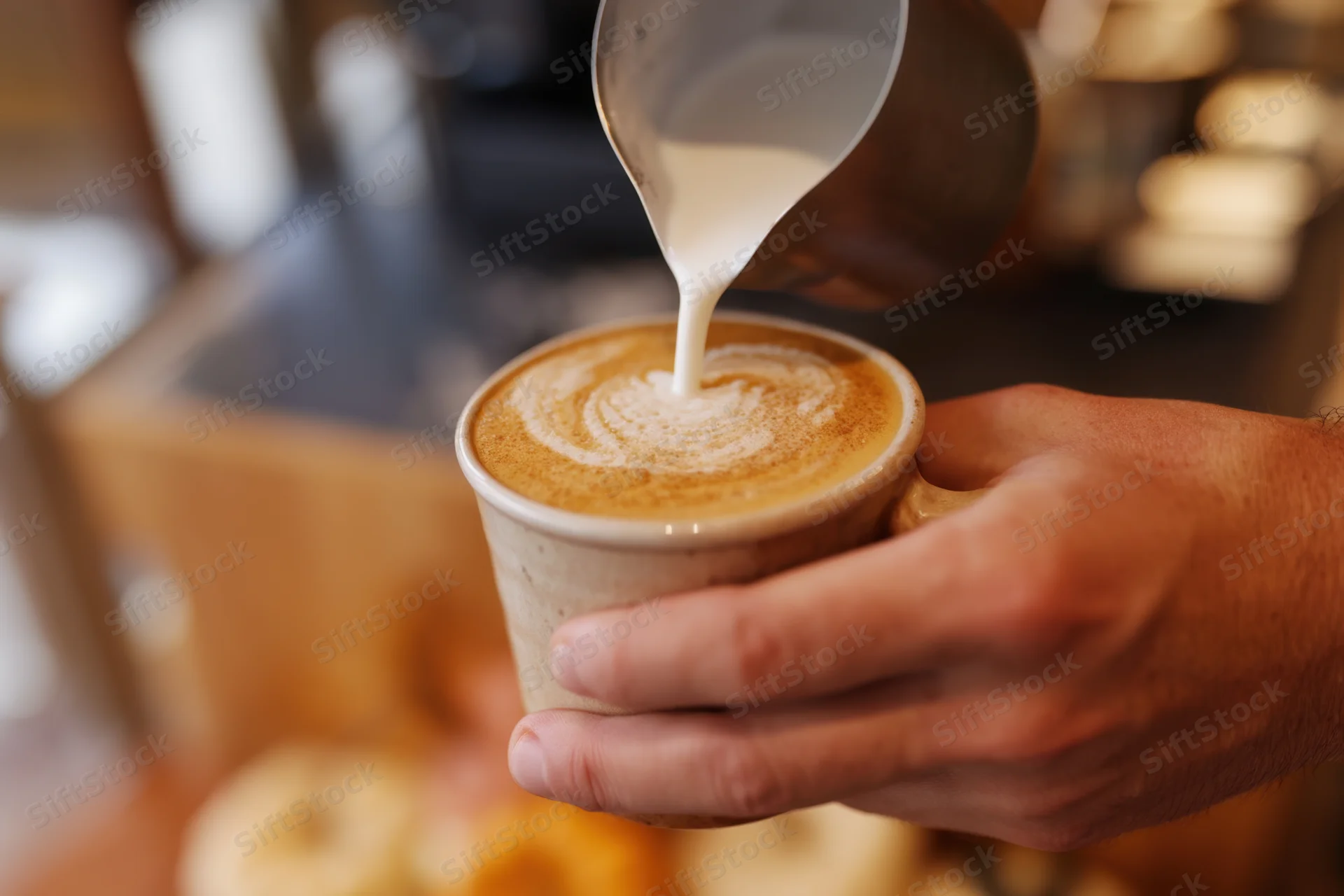 Barista pouring frothed milk into a pumpkin spice latte in a ceramic cup
