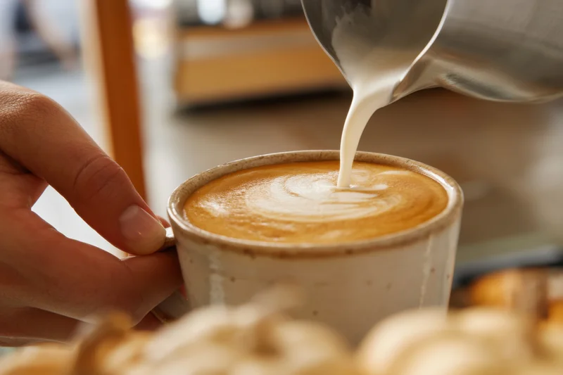 Hand pouring frothed milk into a ceramic cup of latte in a café setting