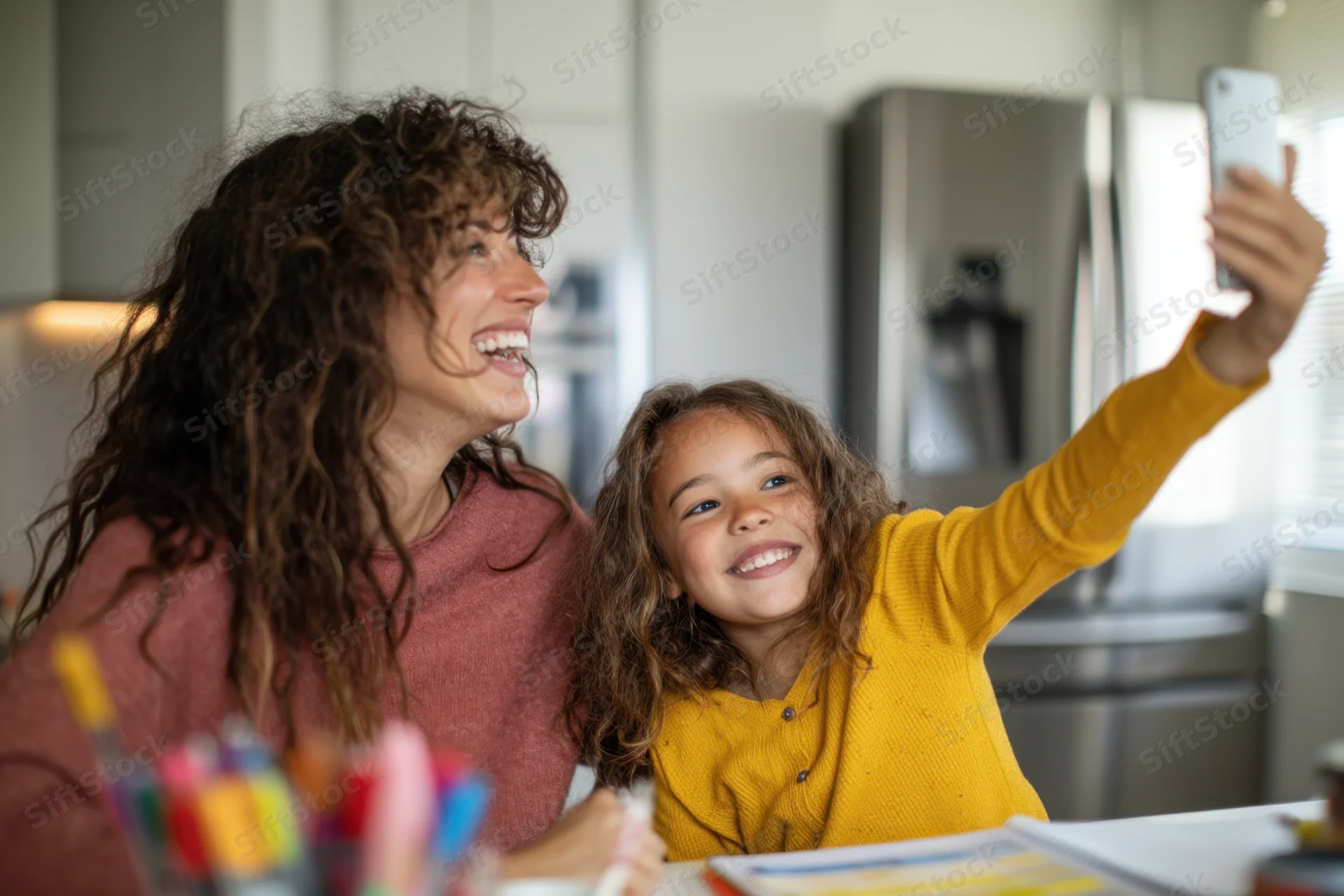 Mother and daughter laughing while taking a selfie at kitchen table