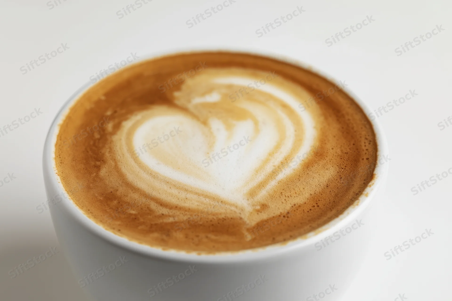 Latte art heart design on creamy coffee surface in white ceramic cup