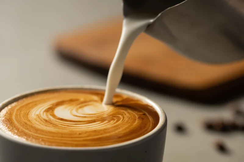 Milk being poured into a gray ceramic cup to create latte art swirls on coffee foam