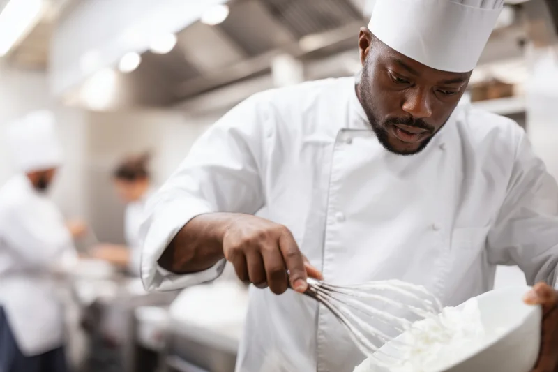Male chef mixing cream in a bowl with a whisk in a professional kitchen