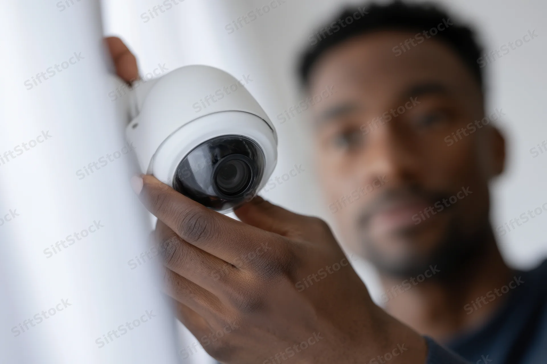 Man installing security camera on white wall indoors