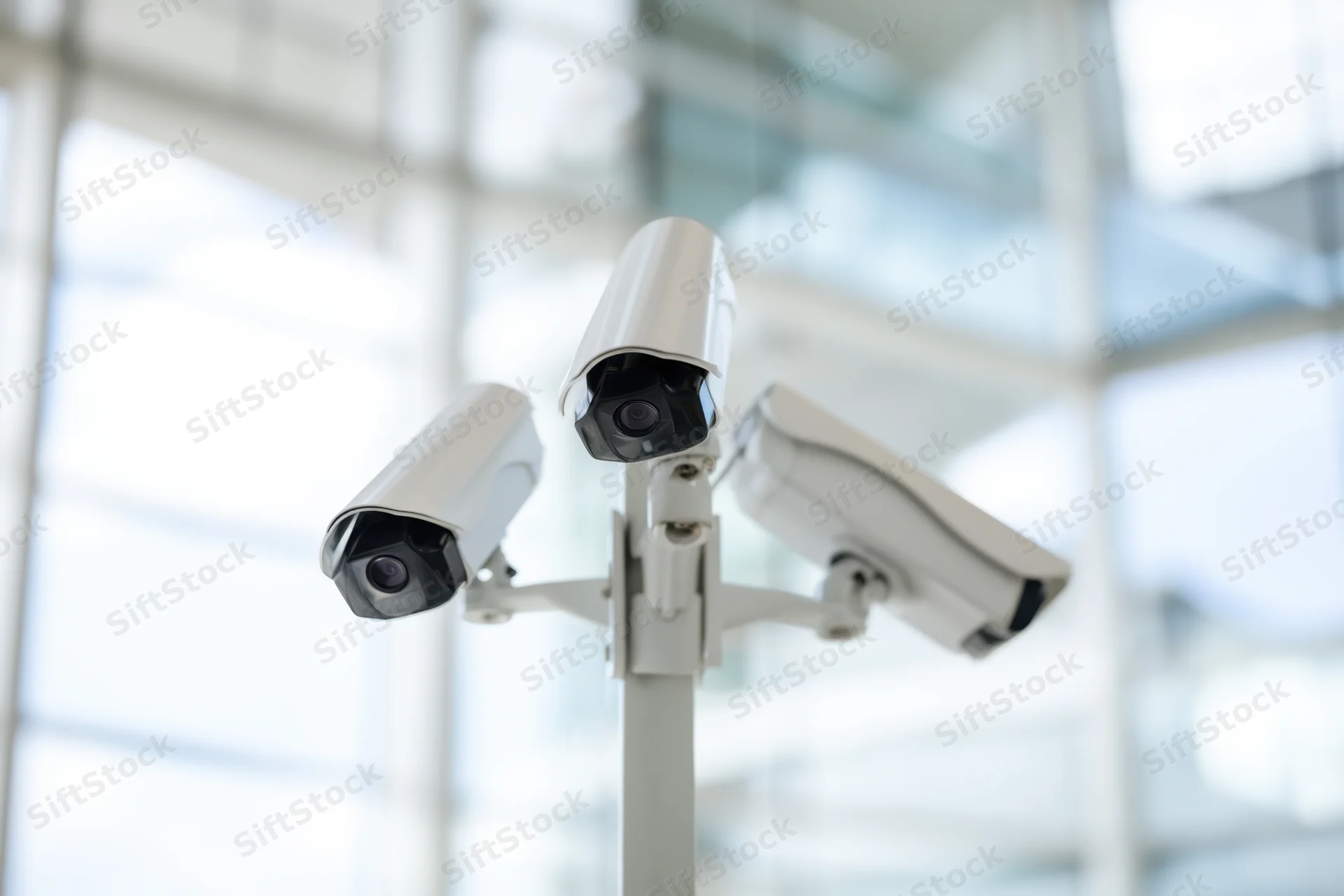 Three white security cameras mounted on a pole indoors with blurred background