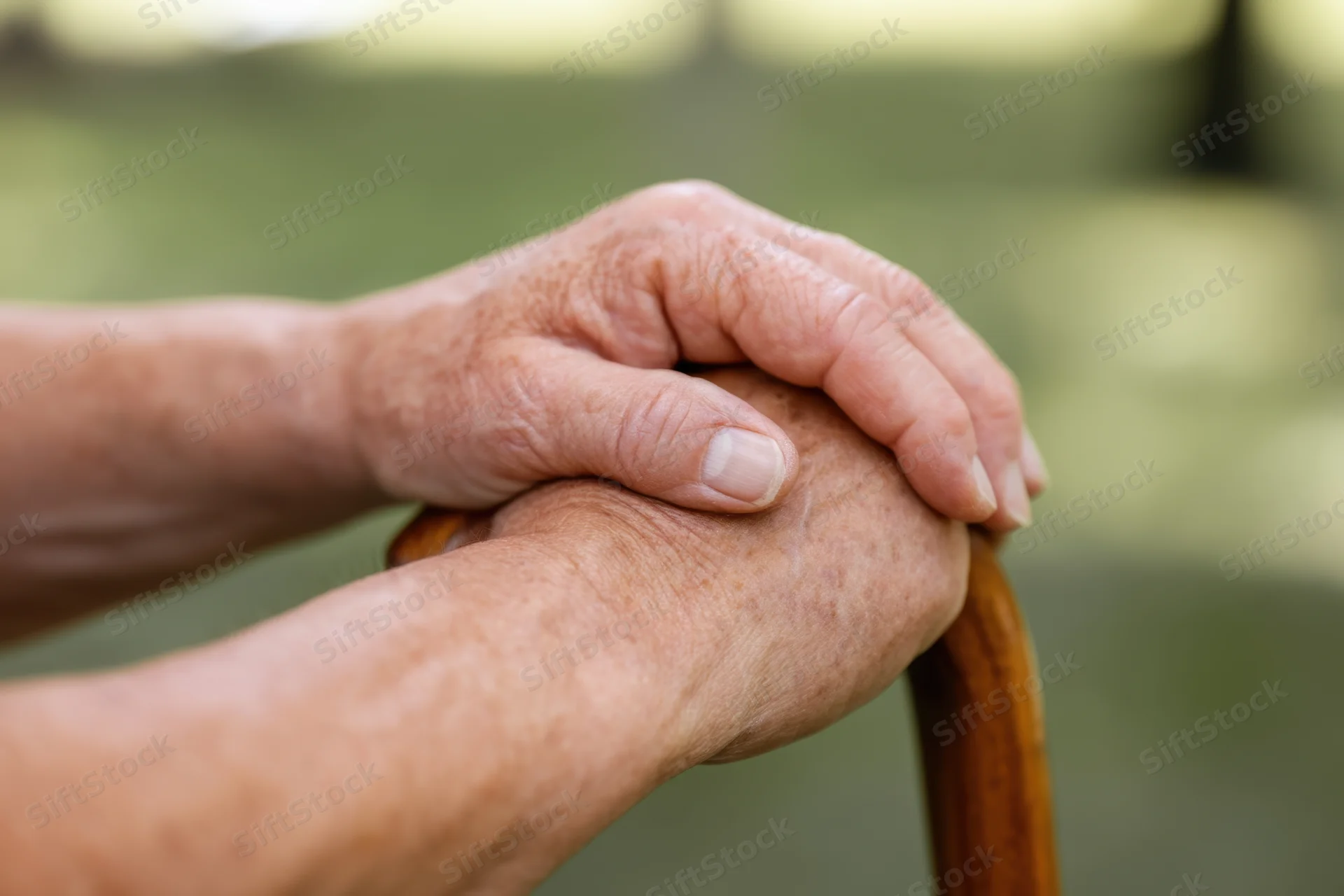 Elderly hands gripping a wooden cane outdoors