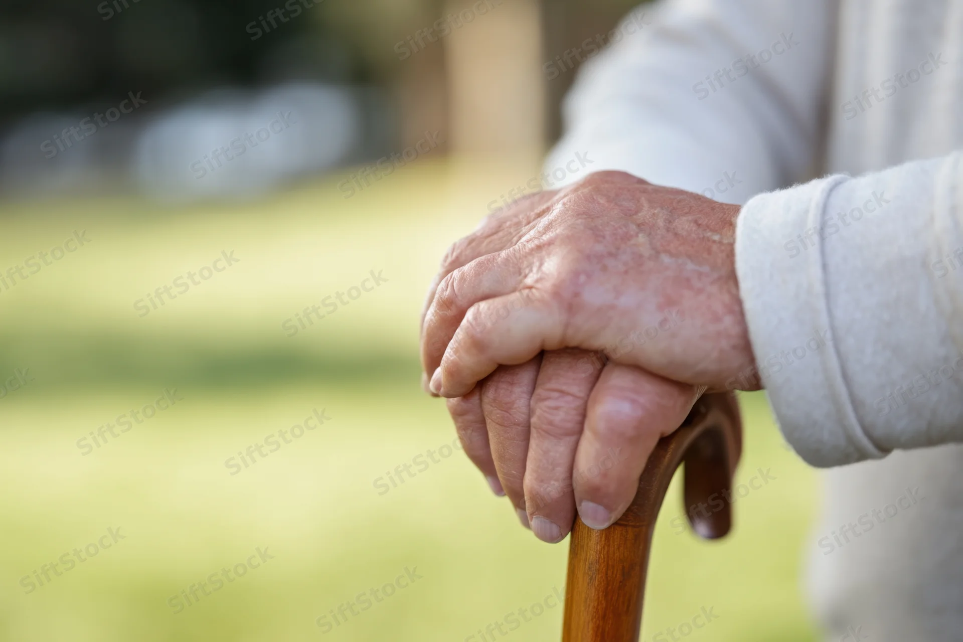 Senior hands gripping a wooden cane outdoors in a garden setting