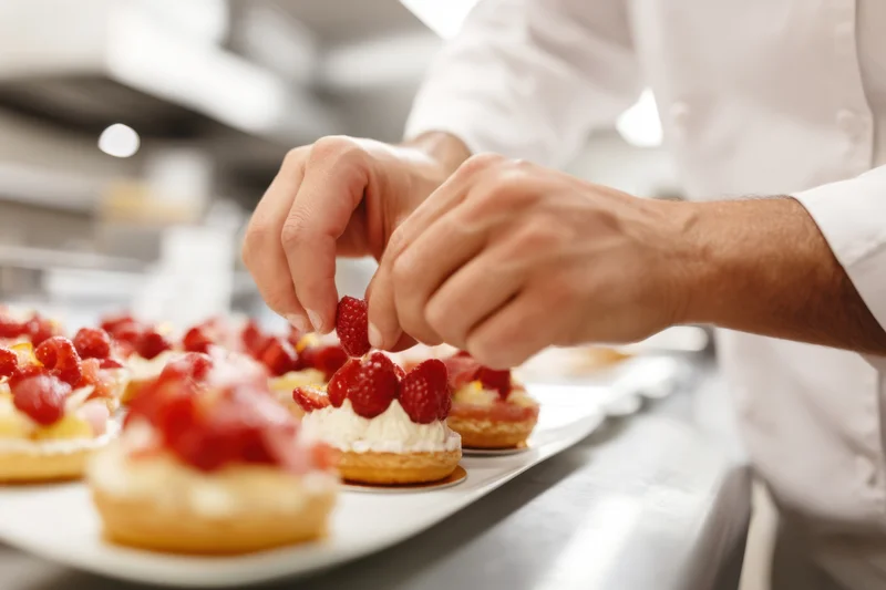 Pastry chef placing fresh raspberries on cream-filled pastries in a kitchen