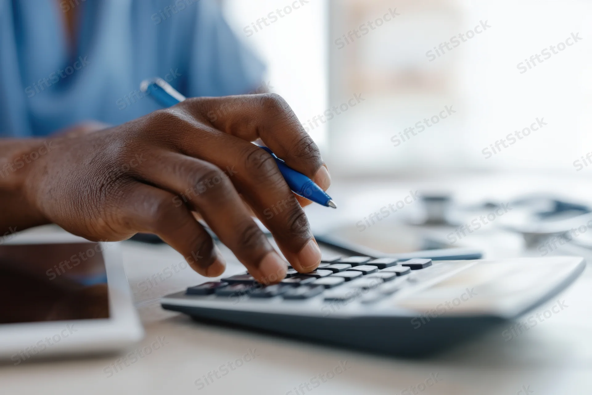 Hand using calculator while holding pen on office desk
