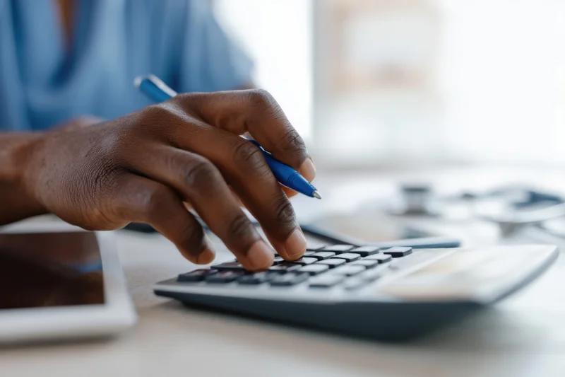 Hand using calculator while holding pen on office desk