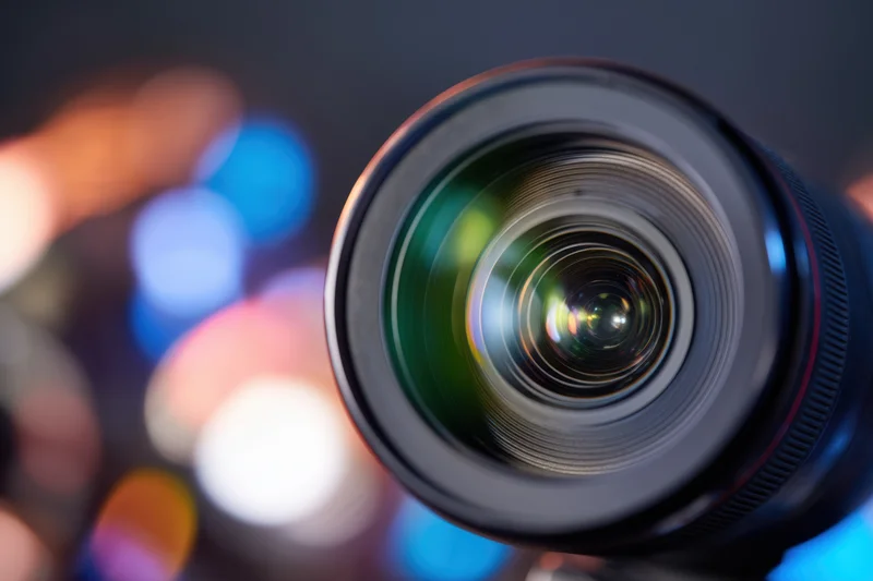 Closeup of a professional camera lens with intricate glass elements and colorful bokeh background