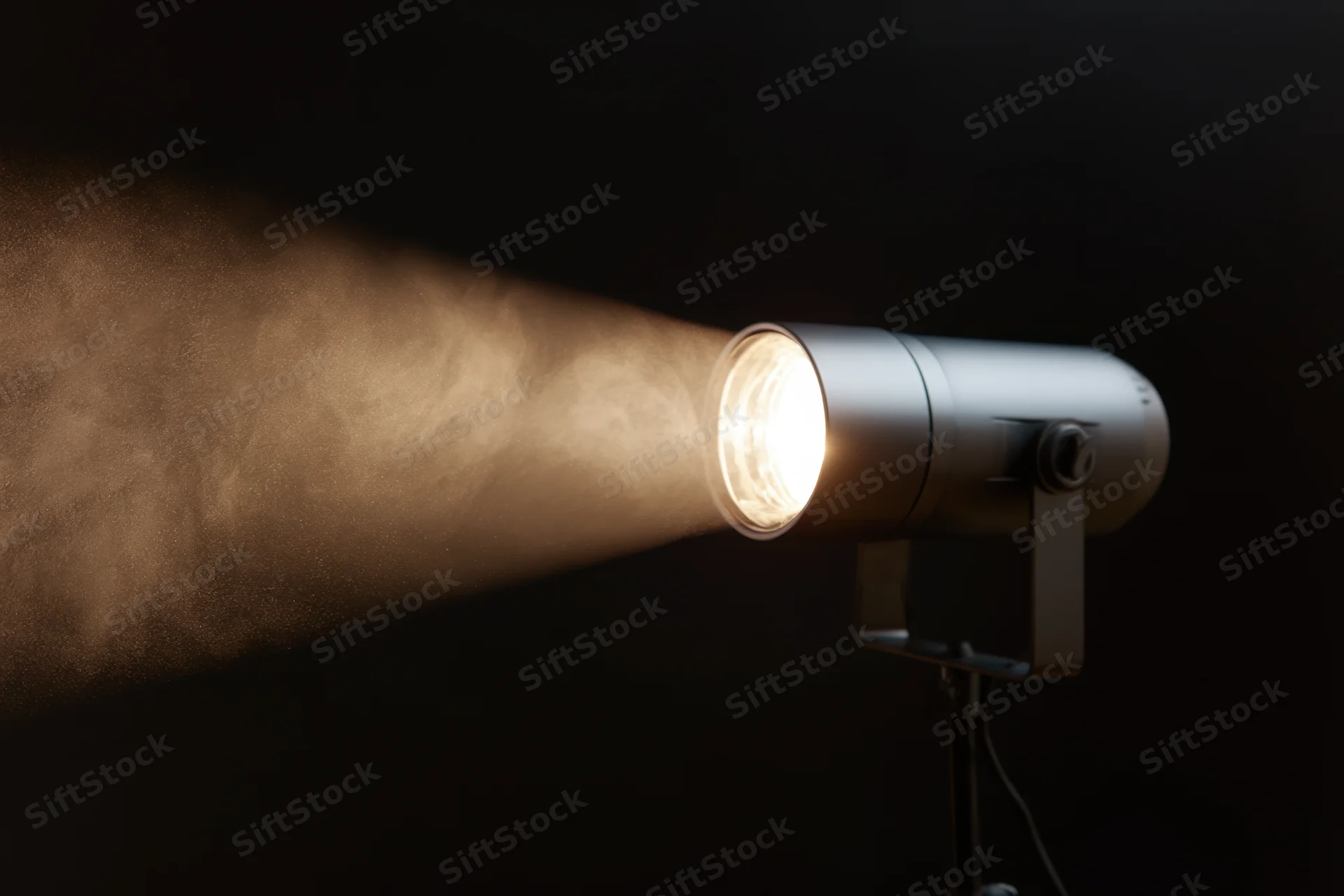 Professional studio spotlight emitting a focused beam of warm light through haze against a dark background