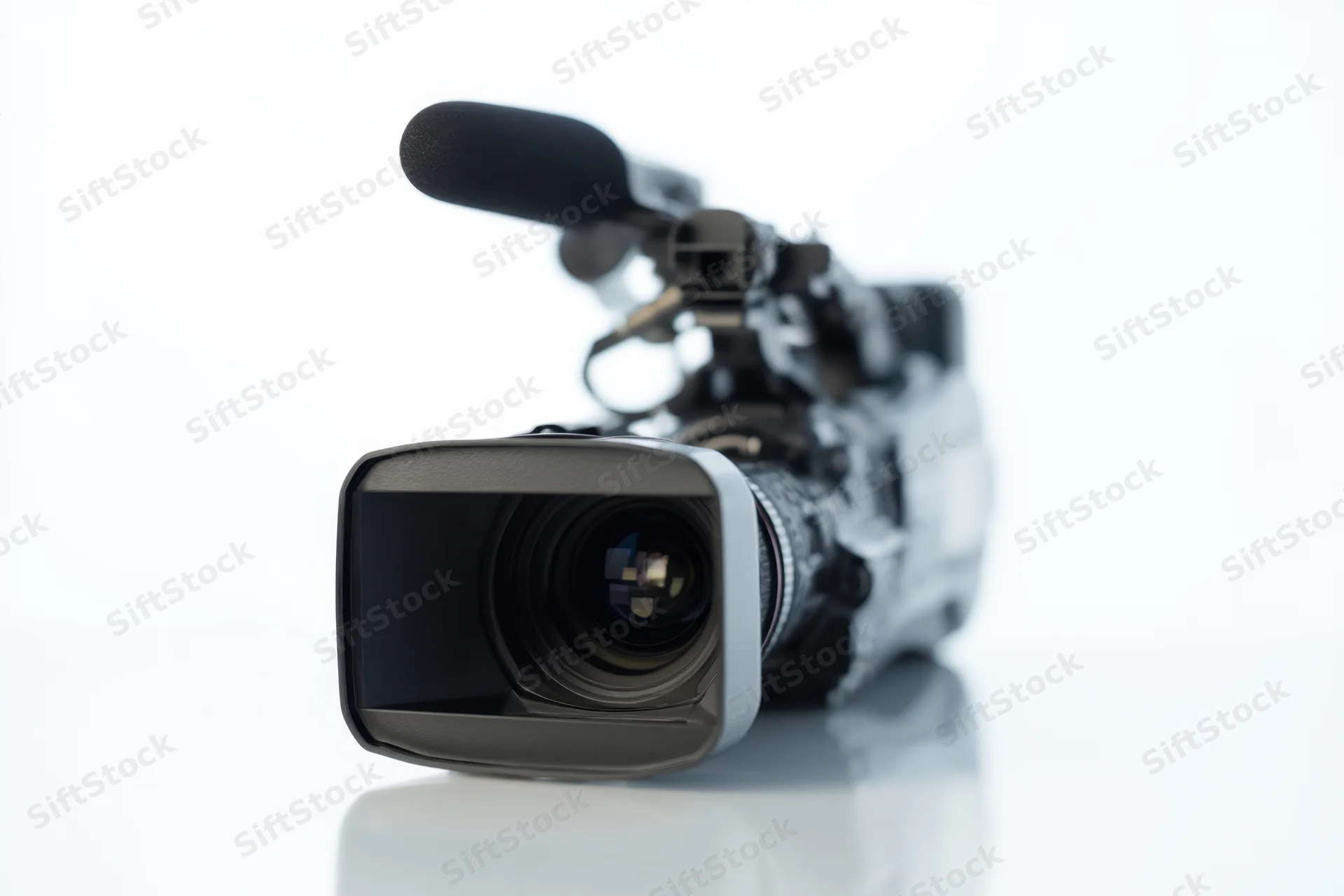 Professional video camera with large lens and microphone on reflective white surface