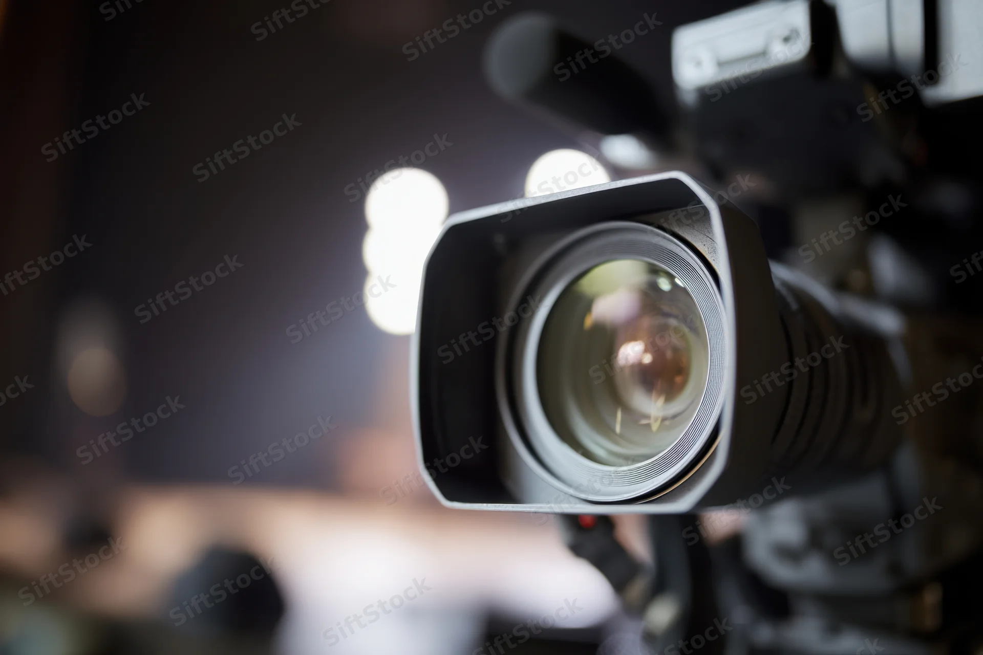 Professional video camera lens in closeup focus with blurred studio lights in background