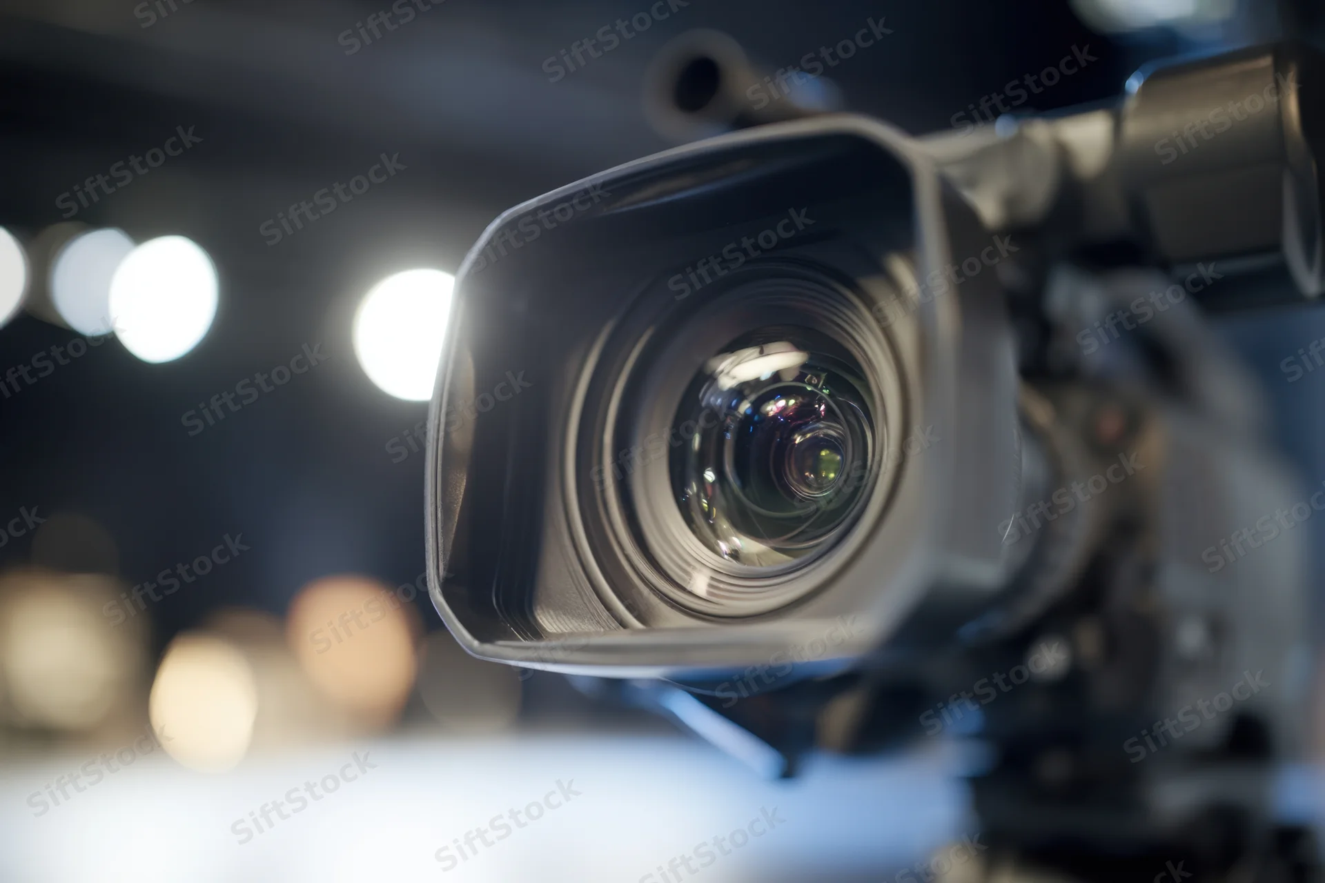 Professional video camera lens in closeup focus with studio lights blurred in background
