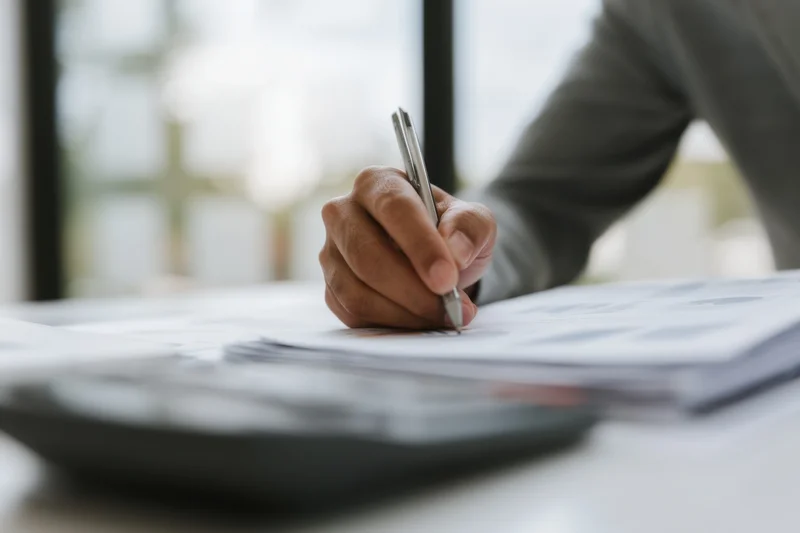 Hand writing on document with pen at office desk
