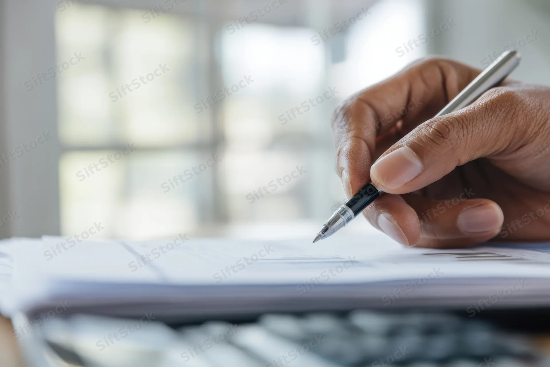 Hand writing on document with pen in office workspace