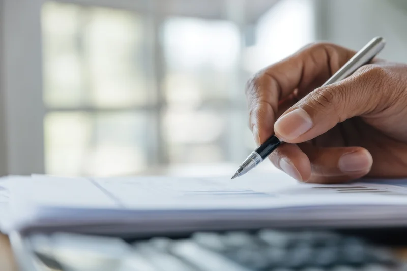Hand writing on document with pen in office workspace