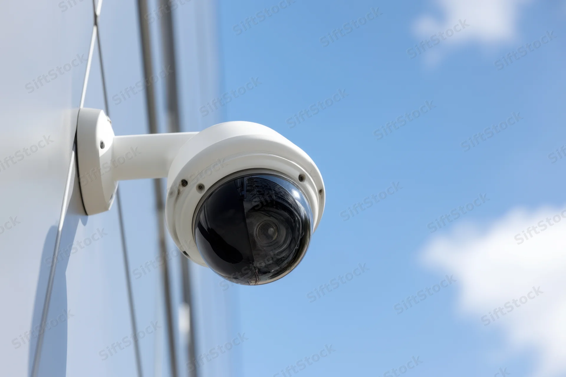 White dome security camera mounted on sleek building exterior under clear blue sky