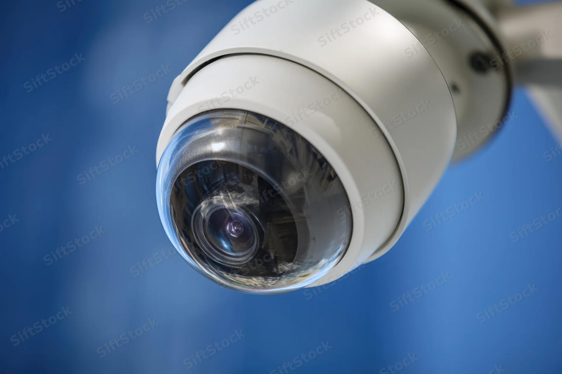 White dome security camera mounted on a wall with blue background