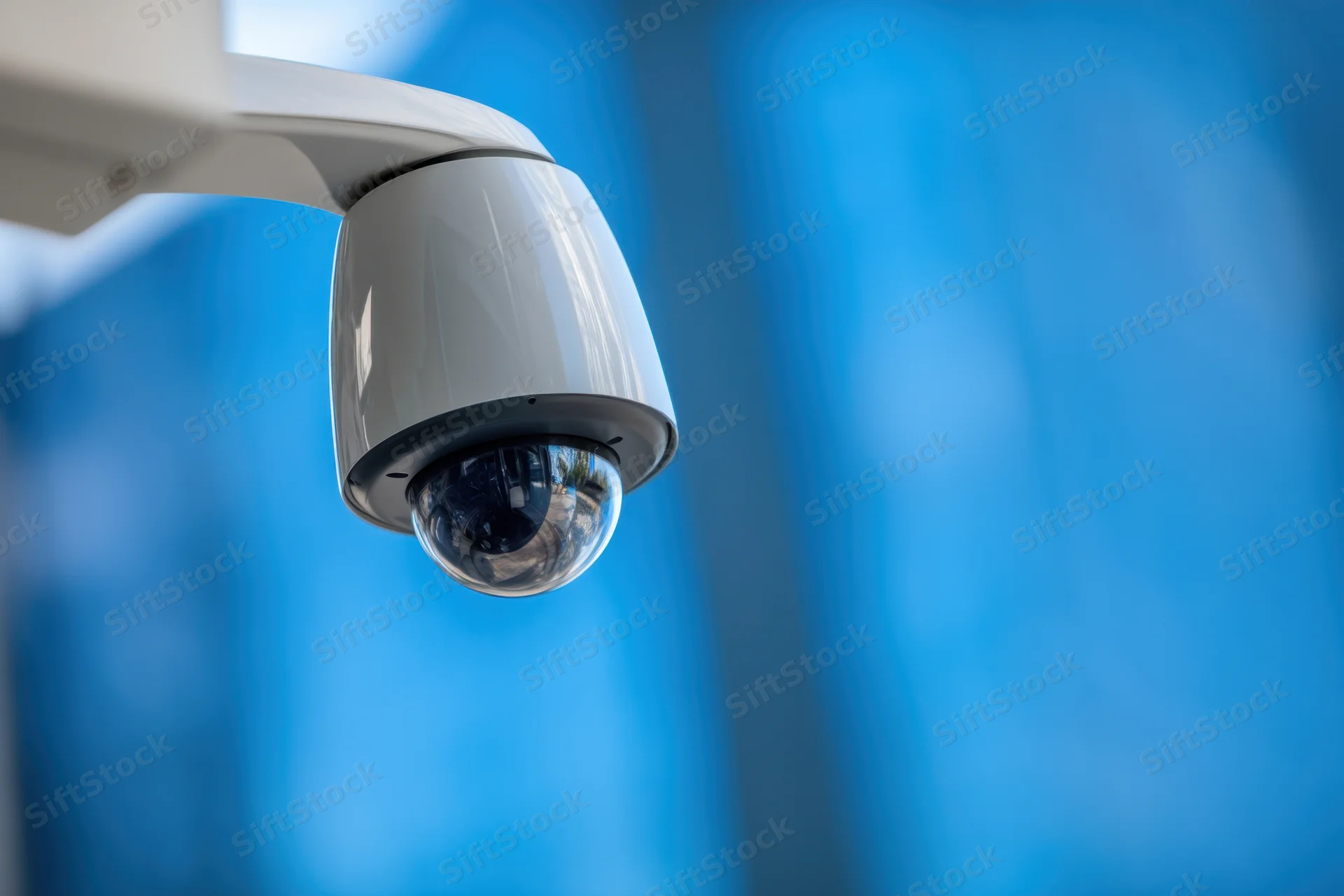 White dome security camera mounted on a wall with blue blurred background