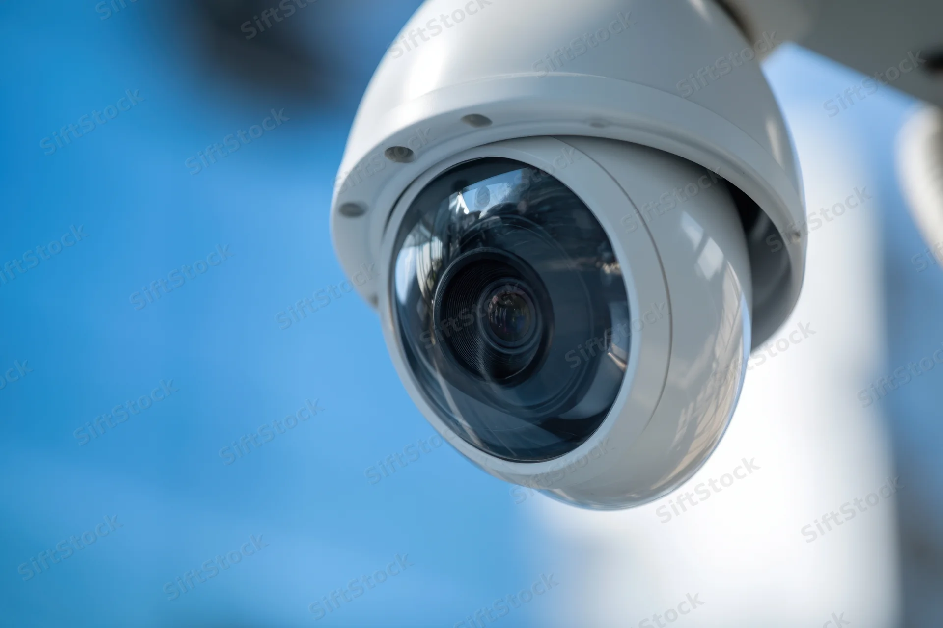 White dome security camera mounted on a wall against a blue sky background