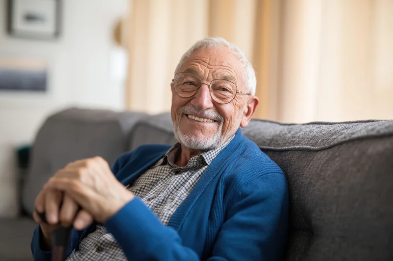 Senior man smiling while sitting on a gray sofa in a living room