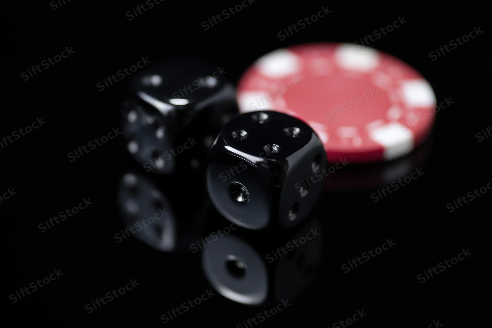 Black glossy casino dice and red poker chip arranged on reflective dark surface
