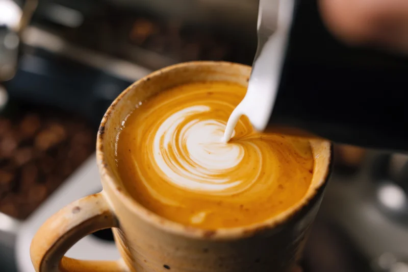 Barista pouring steamed milk into a ceramic mug to create latte art in a coffee shop setting