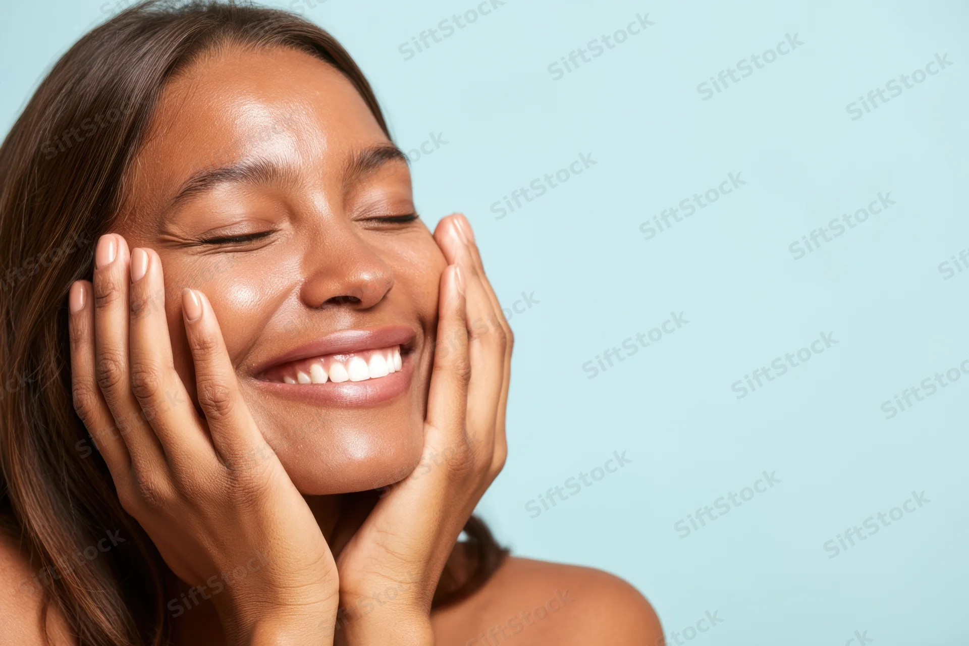 Smiling woman with closed eyes holding her face in hands against blue background