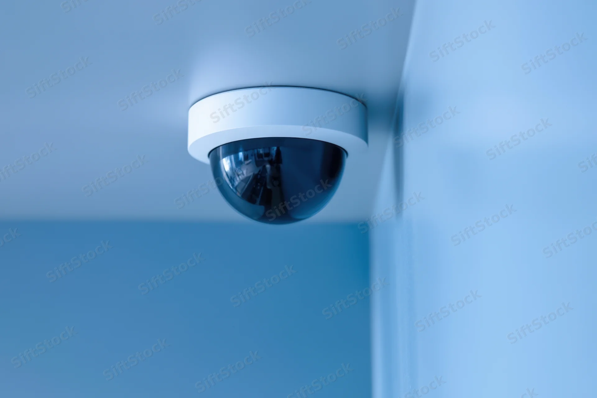 Dome surveillance camera mounted on ceiling in corner of room