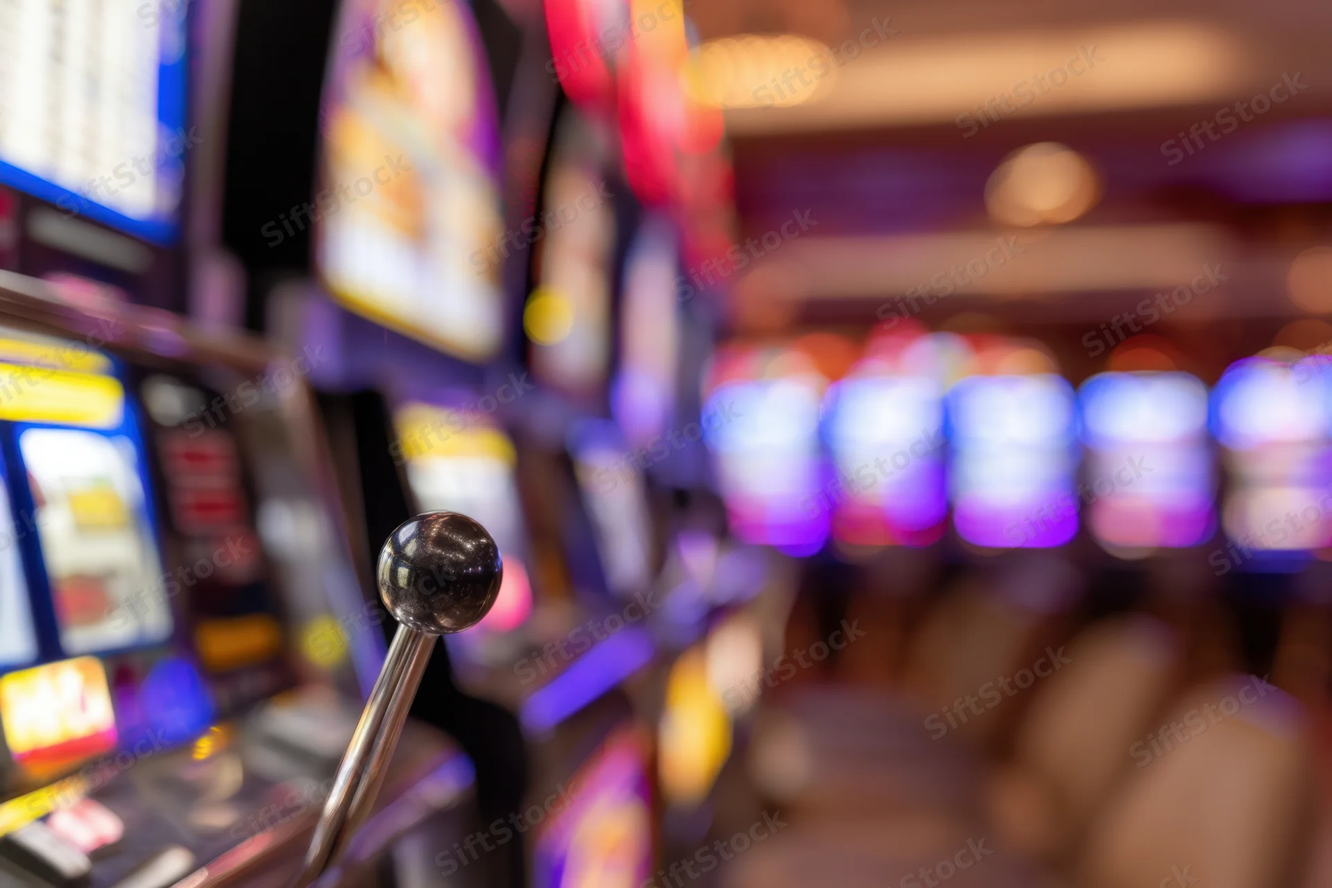 Closeup of a slot machine lever in a vibrant casino interior with blurred rows of glowing machines in the background
