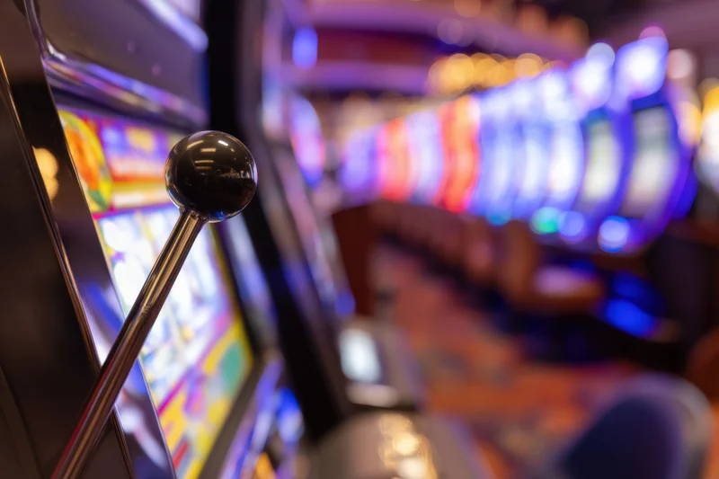 Close-up of a slot machine lever in a vibrant casino interior with blurred neon lights in the background