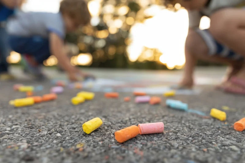 Children playing with colorful chalk on sidewalk during daytime outdoor activity