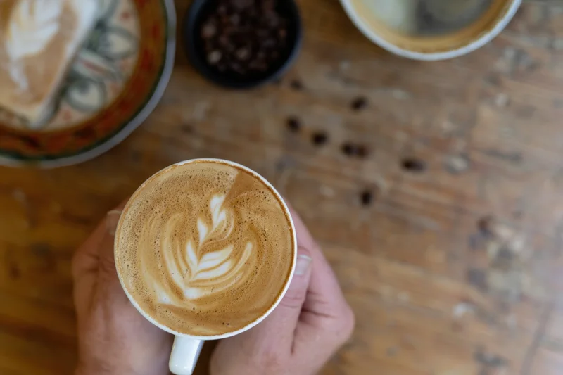 Hands holding a warm latte with leaf-shaped latte art on a wooden table