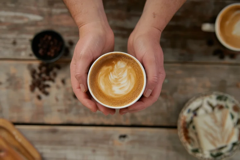 Hands holding a latte with latte art on a wooden table