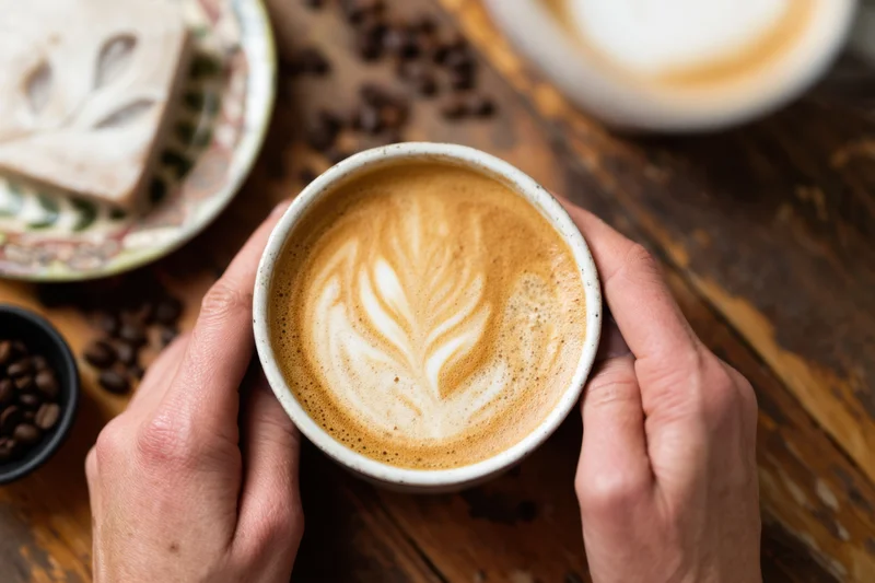 Hands holding a latte with leaf-shaped latte art on a wooden table