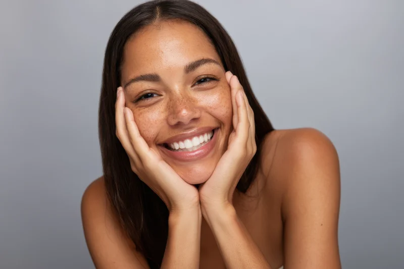 Woman smiling with hands on cheeks in studio portrait