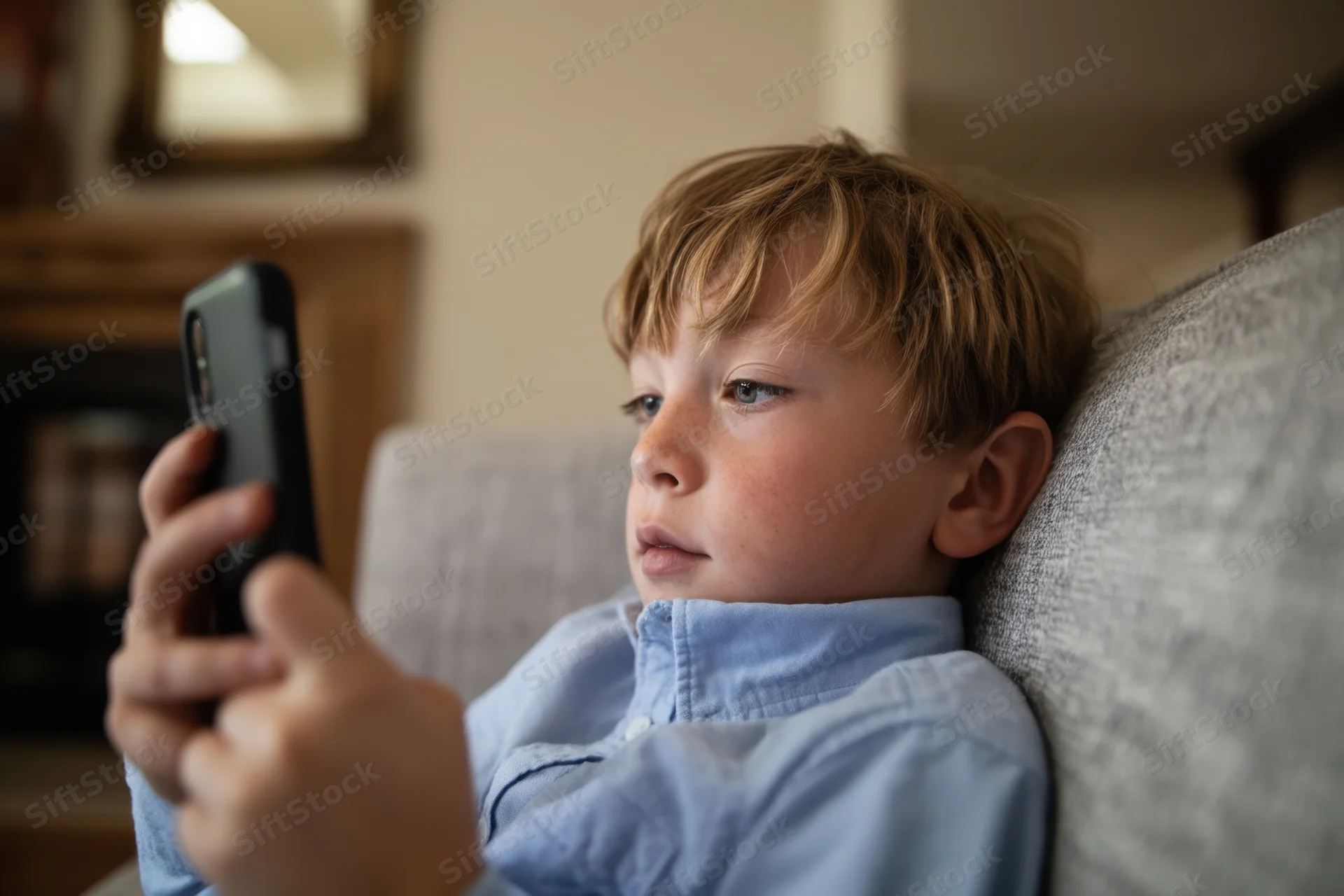 Young boy concentrating on smartphone while reclining on sofa at home