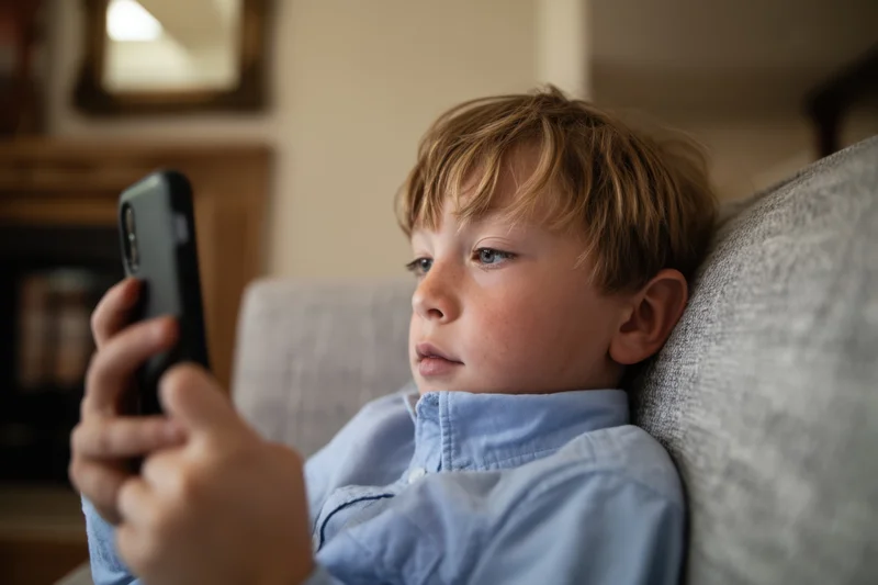Young boy concentrating on smartphone while reclining on sofa at home